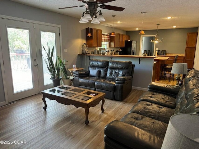 living room featuring ceiling fan, light wood-type flooring, a textured ceiling, and french doors