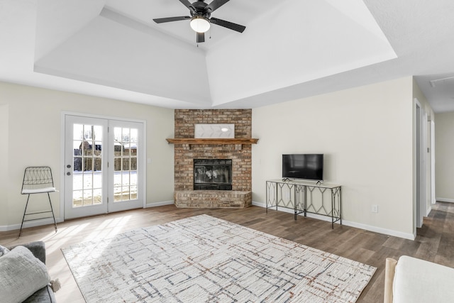 unfurnished living room with a brick fireplace, ceiling fan, dark hardwood / wood-style floors, and a tray ceiling