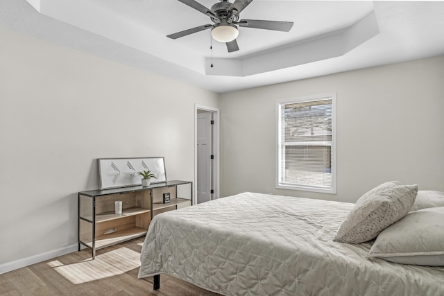 bedroom featuring ceiling fan, a raised ceiling, and wood-type flooring