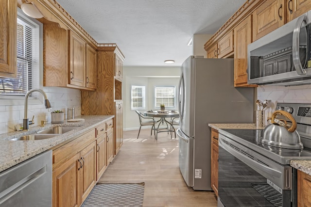 kitchen featuring light stone countertops, sink, stainless steel appliances, and light wood-type flooring