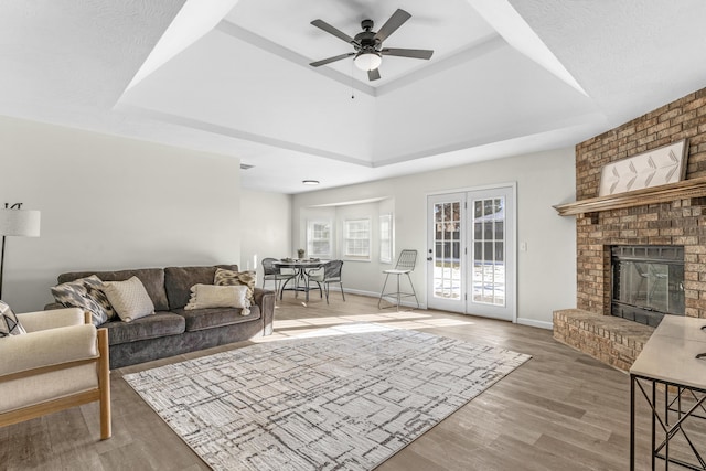 living room featuring a fireplace, wood-type flooring, a tray ceiling, and ceiling fan