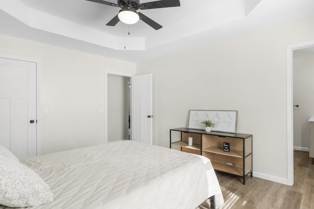 bedroom with hardwood / wood-style floors, a raised ceiling, and ceiling fan