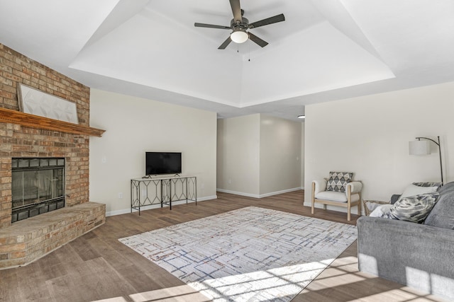 living room with a raised ceiling, ceiling fan, light hardwood / wood-style floors, and a brick fireplace