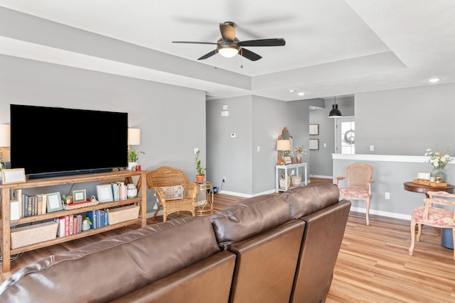 living room featuring light hardwood / wood-style flooring, a raised ceiling, and ceiling fan