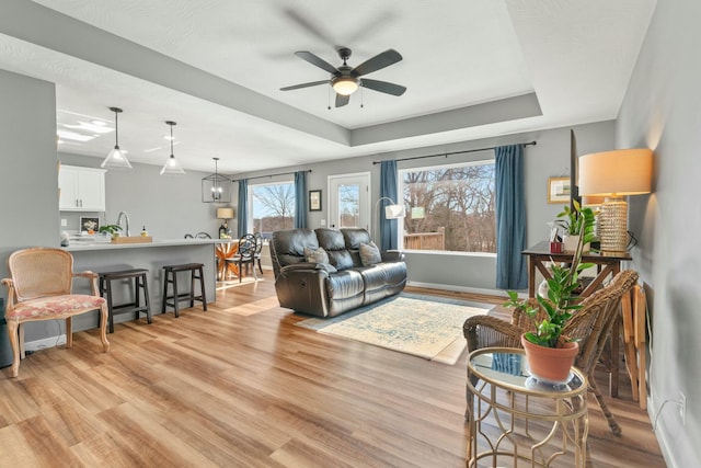 living room with sink, a tray ceiling, ceiling fan, and light wood-type flooring