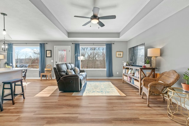 living room featuring a raised ceiling, ceiling fan with notable chandelier, and light wood-type flooring