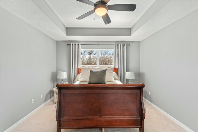 carpeted bedroom with ceiling fan and a tray ceiling