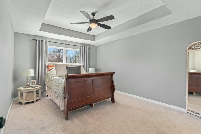 bedroom featuring light colored carpet, a raised ceiling, and ceiling fan