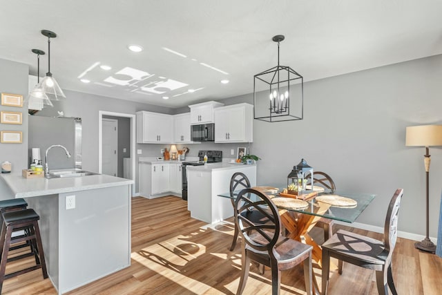 kitchen with a kitchen bar, black appliances, light hardwood / wood-style flooring, kitchen peninsula, and white cabinets