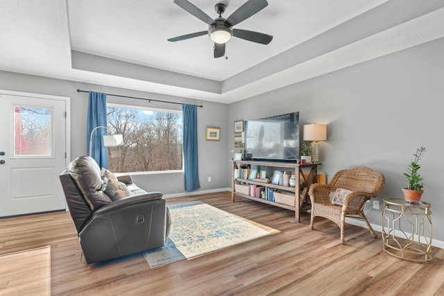 living room with wood-type flooring, ceiling fan, and a tray ceiling