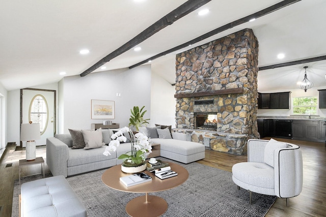 living room featuring a stone fireplace, hardwood / wood-style floors, lofted ceiling with beams, and an inviting chandelier