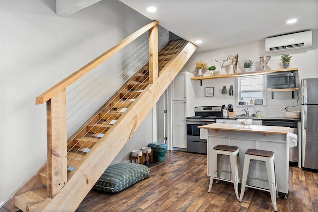 kitchen with a wall unit AC, dark hardwood / wood-style flooring, a kitchen bar, and stainless steel appliances