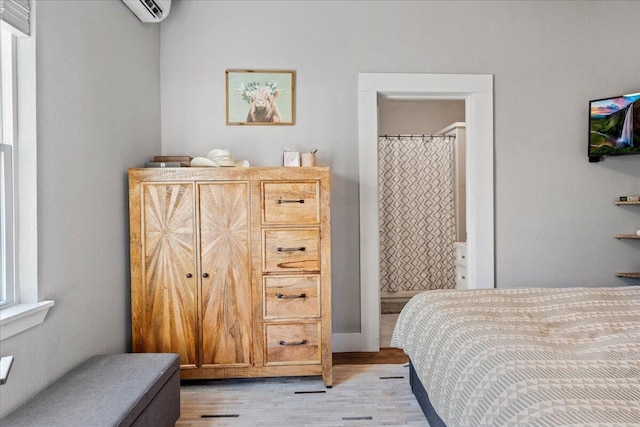 bedroom with light hardwood / wood-style flooring, a wall mounted AC, and ensuite bath