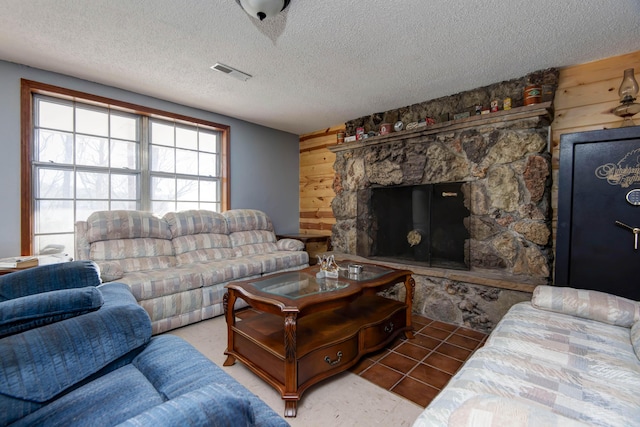 tiled living room with wood walls, a fireplace, and a textured ceiling