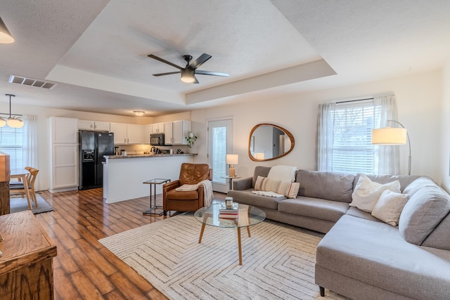 living room featuring light hardwood / wood-style flooring, a raised ceiling, and ceiling fan