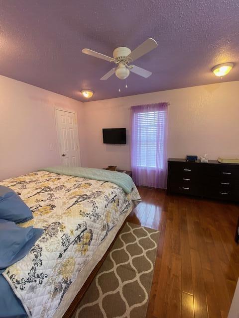 bedroom with a textured ceiling, ceiling fan, and dark hardwood / wood-style floors