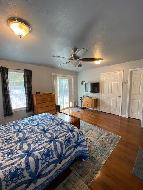 bedroom with multiple windows, ceiling fan, dark wood-type flooring, and a textured ceiling