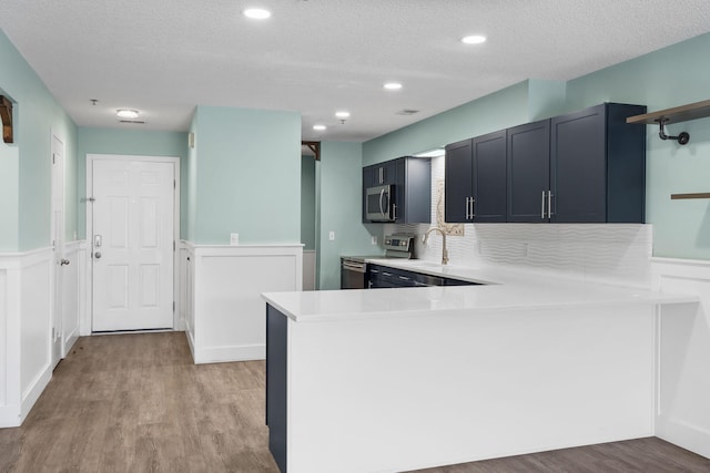 kitchen with a textured ceiling, light wood-type flooring, kitchen peninsula, and stainless steel appliances