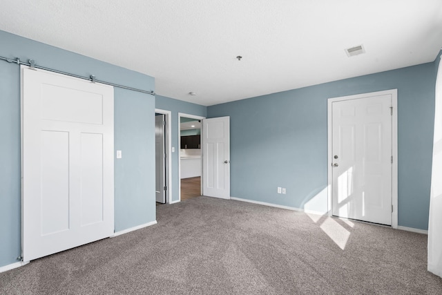 unfurnished bedroom featuring a barn door and carpet floors