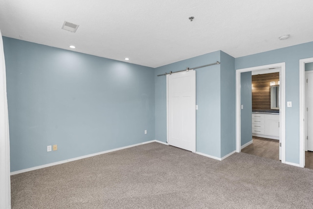 unfurnished bedroom featuring ensuite bathroom, a barn door, carpet, and a closet