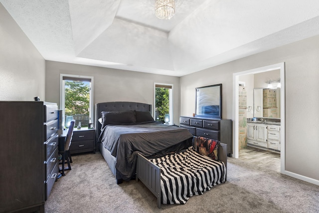 bedroom with light colored carpet, multiple windows, a tray ceiling, and ensuite bath