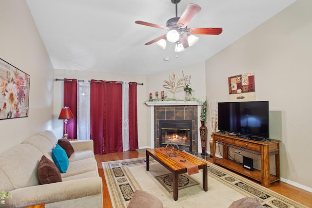 living room featuring a tiled fireplace, ceiling fan, and wood-type flooring