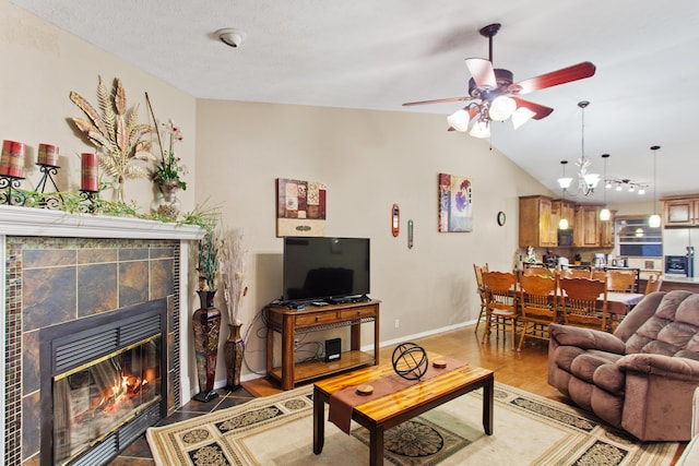 living room with ceiling fan with notable chandelier, lofted ceiling, a textured ceiling, and a tile fireplace