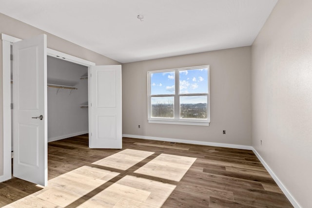 unfurnished bedroom with a closet, a spacious closet, and dark hardwood / wood-style flooring