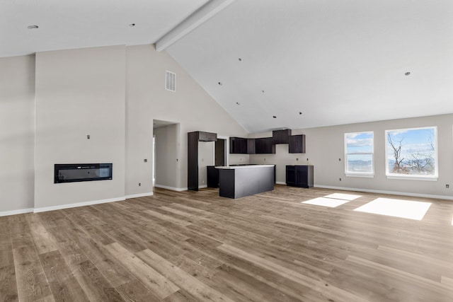 unfurnished living room with beam ceiling, light wood-type flooring, and high vaulted ceiling