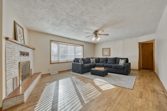 living room with a brick fireplace, ceiling fan, and light hardwood / wood-style floors