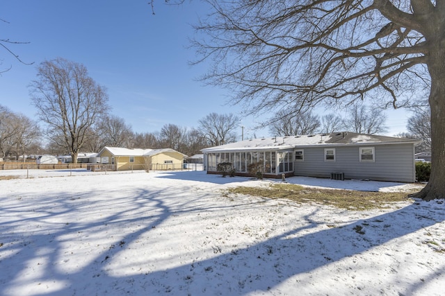 snow covered back of property with cooling unit and a sunroom