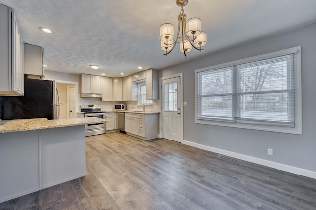 kitchen with sink, light stone counters, hanging light fixtures, a notable chandelier, and appliances with stainless steel finishes