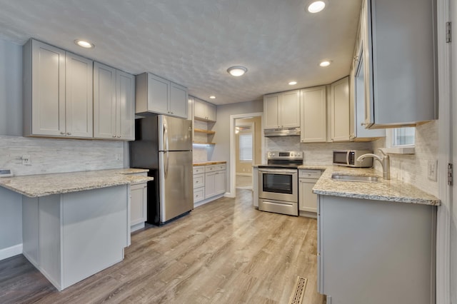 kitchen with light stone counters, appliances with stainless steel finishes, light hardwood / wood-style floors, and sink