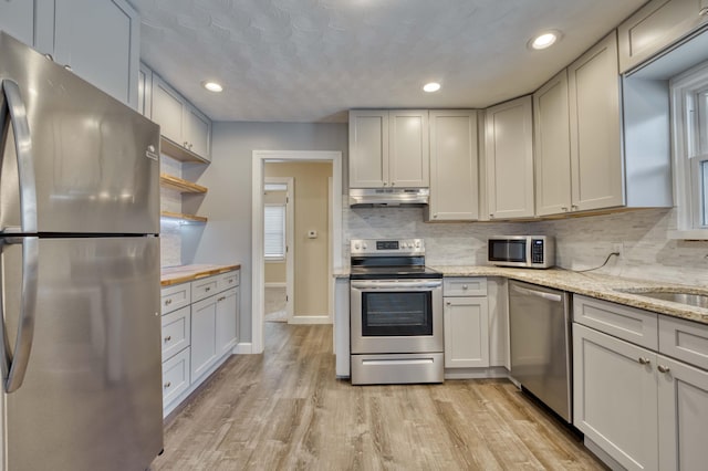 kitchen with stainless steel appliances, sink, white cabinets, light hardwood / wood-style floors, and light stone countertops