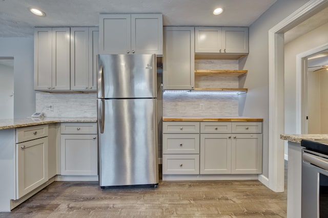 kitchen featuring light hardwood / wood-style flooring, light stone counters, tasteful backsplash, and stainless steel refrigerator