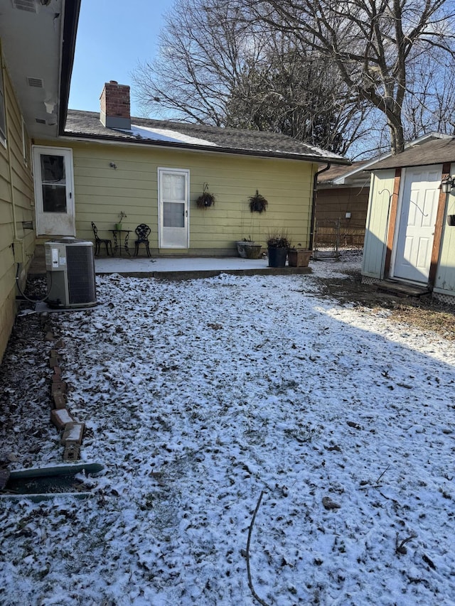 snowy yard with central air condition unit, a storage unit, and a patio