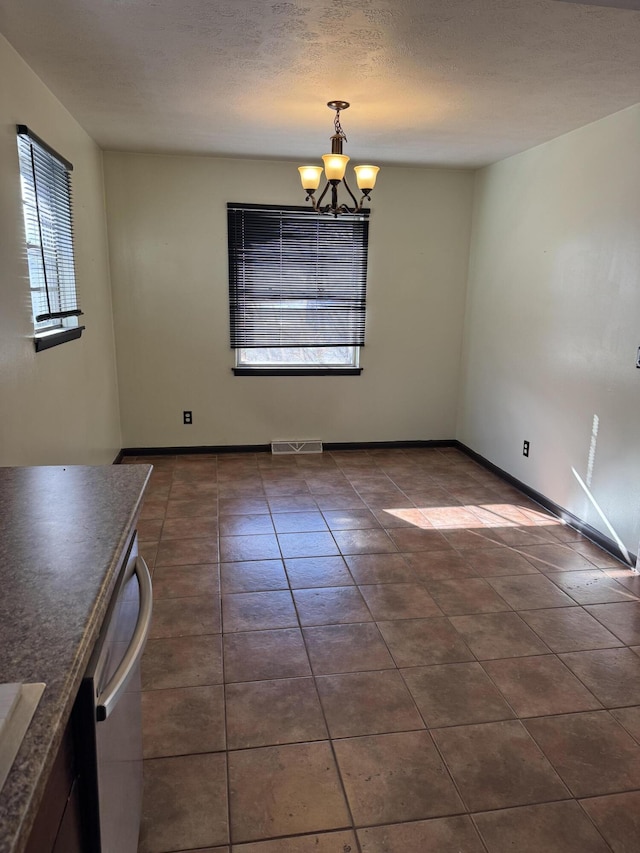 unfurnished dining area featuring sink, an inviting chandelier, dark tile patterned flooring, and a textured ceiling