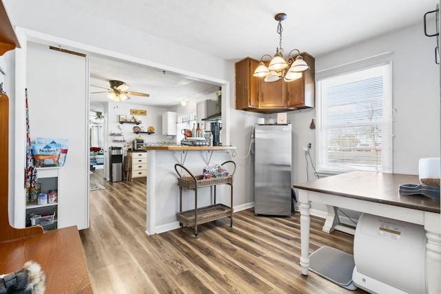 kitchen featuring hardwood / wood-style floors, kitchen peninsula, ceiling fan with notable chandelier, stainless steel refrigerator, and hanging light fixtures