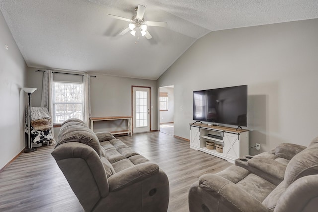 living room featuring lofted ceiling, light wood-type flooring, ceiling fan, and a textured ceiling