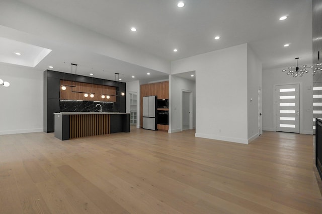 kitchen with a kitchen breakfast bar, a chandelier, light hardwood / wood-style floors, hanging light fixtures, and an island with sink