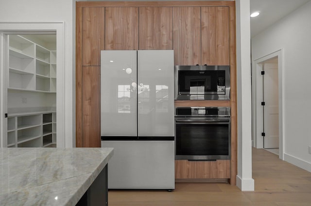 kitchen with stainless steel appliances, light wood-type flooring, and light stone counters