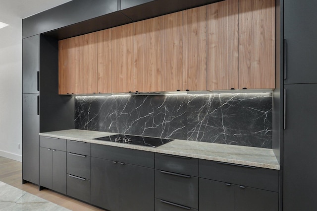 kitchen with black electric cooktop, light stone countertops, light hardwood / wood-style floors, and decorative backsplash