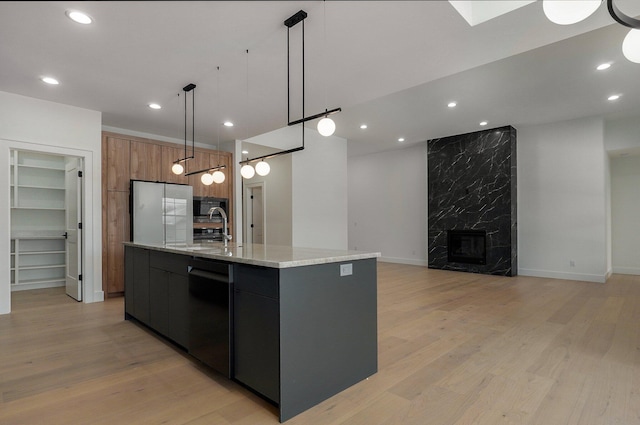 kitchen with a fireplace, dishwasher, a large island with sink, light stone countertops, and pendant lighting