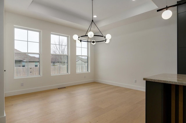 unfurnished dining area with a raised ceiling, a notable chandelier, light wood-type flooring, and a barn door