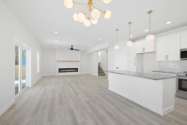 kitchen featuring stainless steel appliances, stone counters, white cabinets, backsplash, and ceiling fan with notable chandelier