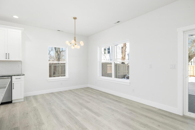 unfurnished dining area with light hardwood / wood-style flooring, an inviting chandelier, and a wealth of natural light