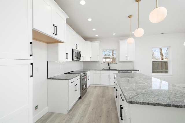 kitchen with appliances with stainless steel finishes, dark stone counters, sink, white cabinetry, and decorative light fixtures