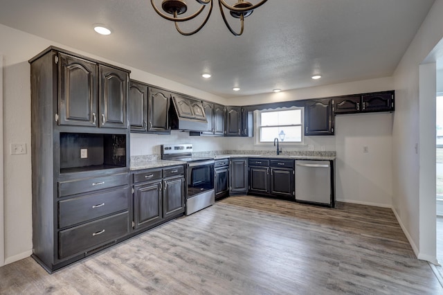 kitchen with custom exhaust hood, appliances with stainless steel finishes, light wood-type flooring, sink, and an inviting chandelier