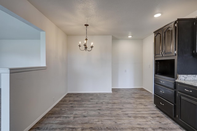 unfurnished dining area with a textured ceiling, a chandelier, and light wood-type flooring