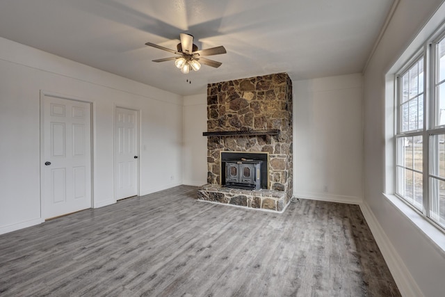 unfurnished living room with wood-type flooring, ceiling fan, and a wood stove